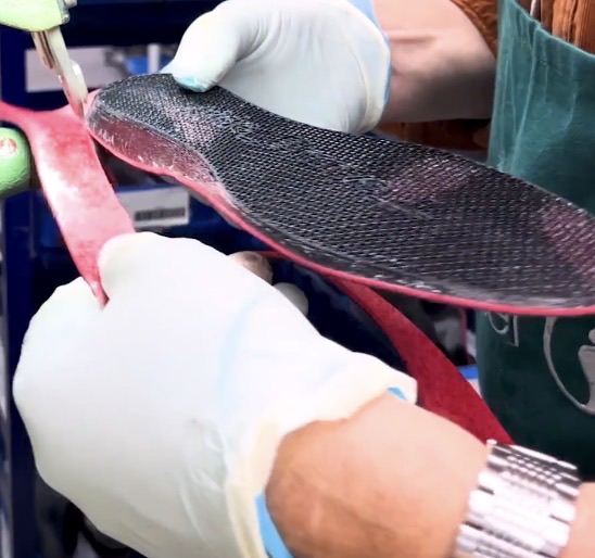 Gloved hands finishing and checking a custom orthotic insole